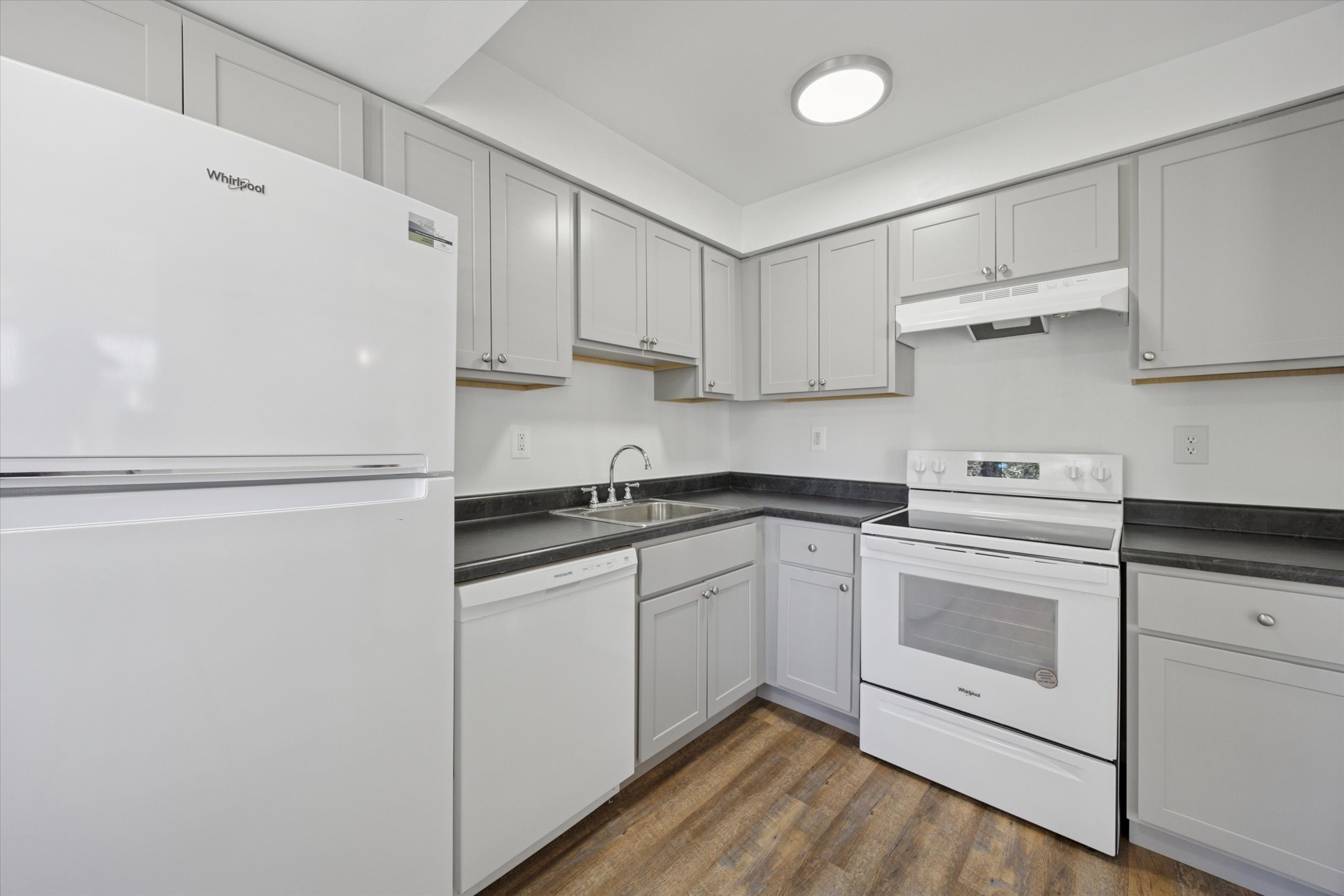 A white refrigerator is in a kitchen with white cabinets.